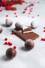 chocolate round candies, chocolate bars and red berries on a gray background and powdered sugar