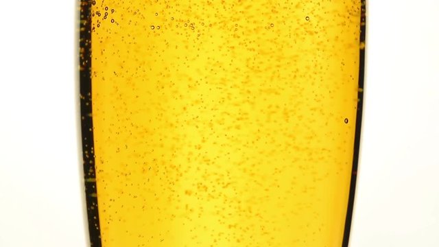 Close up background of pouring beer, sparkling wine or champagne with bubbles in glass, low angle side view, slow motion