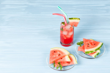 Watermelon lemonade with ice and mint leaves. Homemade lemonade of ripe berry with red and green ripes. Glass of cold watermelon tea. Refreshing summer drink. Cocktail on a wooden background