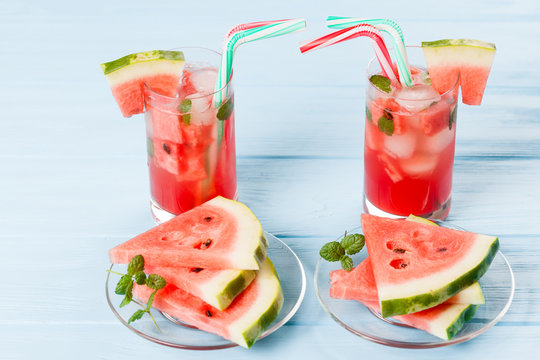 Watermelon lemonade with ice and mint leaves. Homemade lemonade of ripe berry with red and green ripes. Glass of cold watermelon tea. Refreshing summer drink. Cocktail on a wooden background