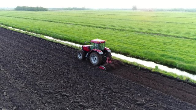 Aerial flying behind tractor flattening the dark just plowed land making it flat so crops can be planted flattening is important part of total cultivation process so plants have steady underground 4k