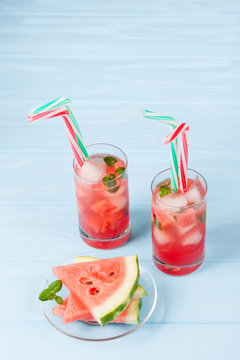 Watermelon lemonade with ice and mint leaves. Homemade lemonade of ripe berry with red and green ripes. Glass of cold watermelon tea. Refreshing summer drink. Cocktail on a wooden background