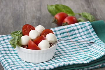Salad Caprese in a white bowl on a gray wooden background. The concept of Mediterranean cuisine.