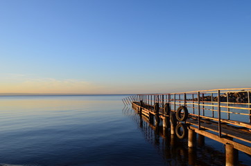 The old pier in the Volga River, lit by the sun at sunset, surrounded by water and clear sky