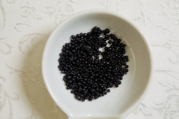 Black caviar in a little bowl on a white background. above view of black dyed salty caviare of halibut fish in glass jar isolated on white background