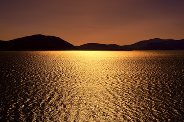 Dark bronze sunset with sun shimmering sun reflections on lake u