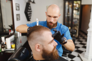 Male professional hairdresser serving client, shaving thick big beard straight razor. Ginger...