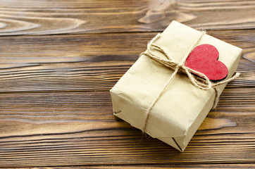 gift box wrapped in kraft paper and red wooden heart on wooden table
