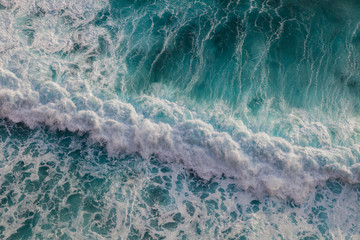 Seashore with rolling waves crashing on rock coast with spray and foam, view from a height of 100 meters, Uluwatu, Bali, Indonesia