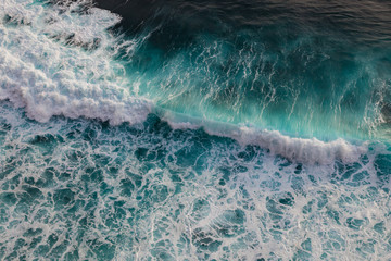 Seashore with rolling waves crashing on rock coast with spray and foam, view from a height of 100 meters, Uluwatu, Bali, Indonesia