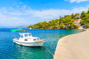 Naklejka na ściany i meble Fishing boat anchoring in Splitska port with beautiful coast in background, Brac island, Croatia