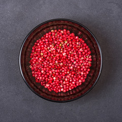 Pink pepper in a bowl on a grey concrete background