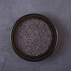 Black sesame seeds in a bowl on a grey concrete background