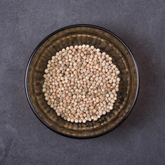 White pepper in a bowl on a grey concrete background