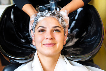 Beautiful young woman with hairdresser washing head at hair salon