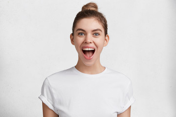 Excited joyful pretty woman with hair knot, rejoices new purchase or big discounts in boutique, isolated over white studio background. Happy female student recieves high grant for wining competiton