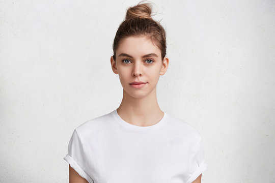 Horizontal shot of confident good looking female student wears casual white t shirt going in gym to have training, works on her constitution. Beautiful young woman models against white background