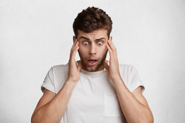 Terrified shocked male looks with bugged eyes down, sees something awful, can`t believe his eyes,...