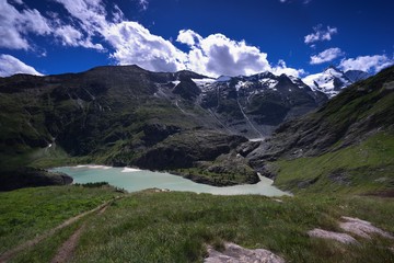 Fototapeta premium High Alpine lake or dam and meadows near Grossglockner mountain in Austria catching water from Pasterze glacier during the summer melting. Picture taken in Austria in Tirol tauern region. 