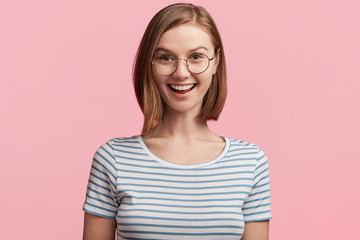 Fototapeta premium Excited positive attractive woman glad to recieve present she dreamt about all life, can`t believe eyes, being thankful to relatives who prepared surprise, wears casual clothes and round glasses