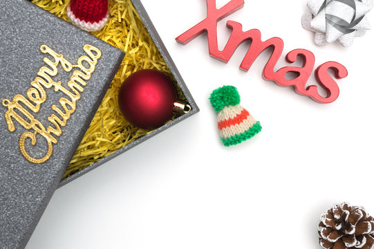 Merry christmas and X-mas text, fur hat, ball, ribbon, pine cone in black gift box with yellow packaging material