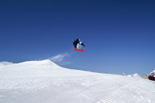 Snowboarder jump in terrain park at ski resort on sunny winter day