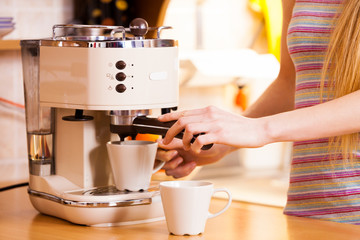 Woman in kitchen making coffee from machine