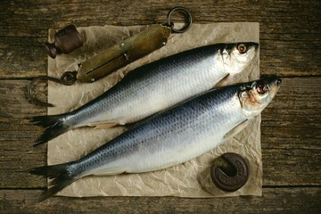 Salted herring fish on an old wooden background with antique hand weights. Rustic style.