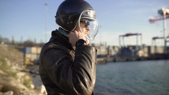 caucasian man motorcyclist wears a helmet near harbor at cold sunny day 