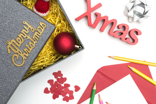 Merry christmas and X-mas text, fur hat, ball, ribbon, christmas card, color pencils, heart in black gift box with yellow packaging material