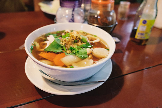 Hot and spicy Thai Dishes. Blurred image of a savoury thick soup made with squid rings, spices and vegetables and crushed peanuts on cafe background. Selective focus