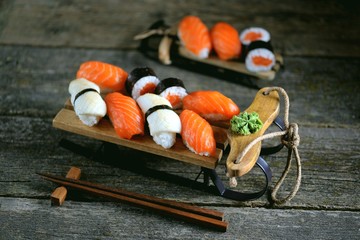 Sushi nigiri and rolls with salmon and fried squid on decorative sleigh, christmas background.