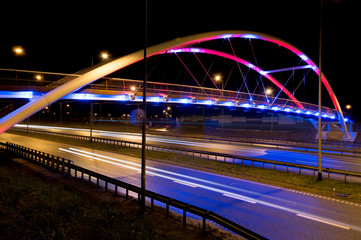 Iluminated bridge over highway by red and blue light.