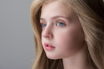 Naklejka premium Feeling sadness. Close-up of face of adorable serious little girl is standing and looking aside thoughtfully. Focus on eyes. Isolated background and copy space