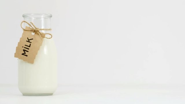 Woman hand turning milk bottle on white background. Dairy products, healthy diet concept