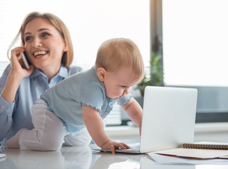 Full length side view happy baby typing in laptop while situating near cheerful mother. She speaking by mobile. Job and family concept