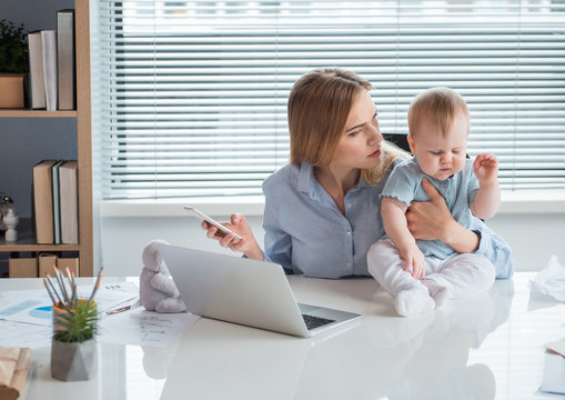Are you ok. Disappointed businesswoman looking at child closing eyes while sitting on table. She working in office. Job and baby concept