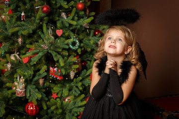 Pray a little girl in a black angel costume, looking with hope for peace. Happy childhood and peace. Christmas, New Year