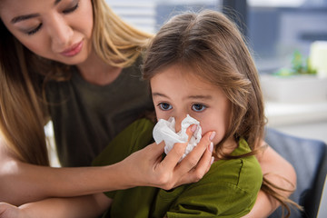 Portrait of cut asian girl blowing snot into the napkin. Her mother is keeping it near her nose with care