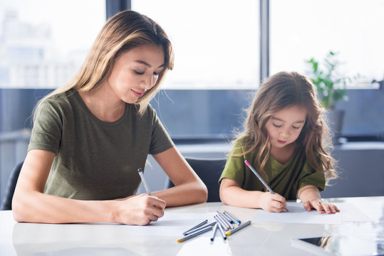 Portrait of cheerful asian family is drawing together at home. They are holding colorful pencils and looking at paper with concentration