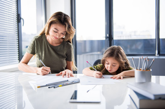 Portrait of happy mother and daughter drawing pictures together. They are sitting at table at home