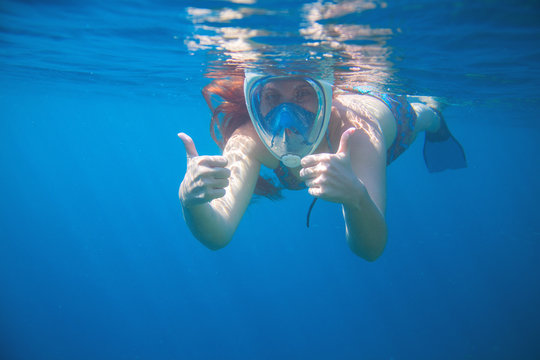 Woman snorkeling showing thumbs. Snorkel in full face mask. Female swim with loose red hair.