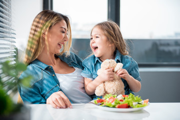 Portrait of excited mother and daughter laughing while having lunch in kitchen