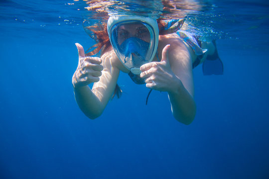 Girl underwater showing thumbs. Snorkeling woman in full face mask.