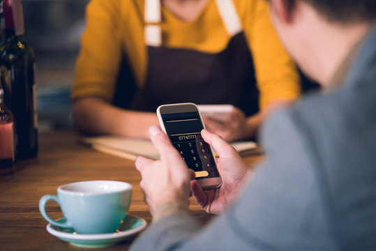 Close up man hands keeping mobile phone while drinking mug of coffee in cafe. He sitting opposite worker. Technology concept