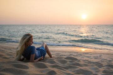 young woman in blue t shirt and jeans short laying on the beach by the sea with mountains and clouds on background