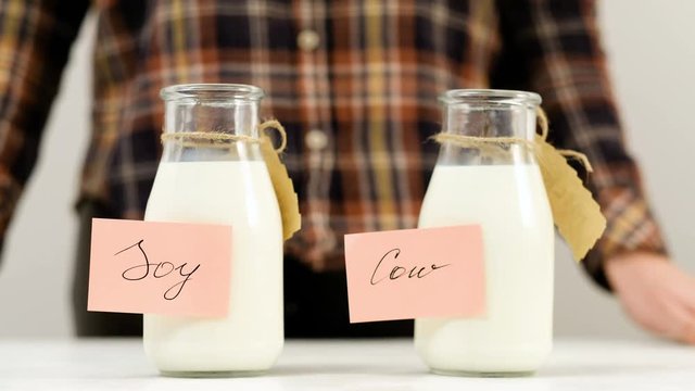 Woman turning two bottles of milk. Soy milk as a substitute of cow milk for vegans.