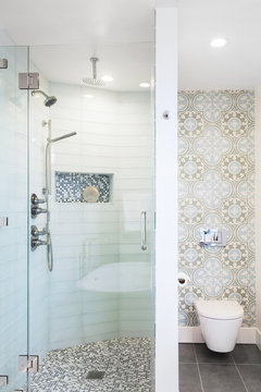 Modern glass shower with mosaic flooring, glass tiles and wallpaper above toilet.