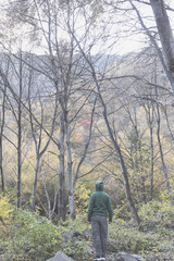 A man in a green dress stands in the face of a colourful forest.
