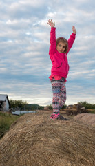 5 year old girl stands on bail of hay with outstretched arms on sheep farm in northern ontario